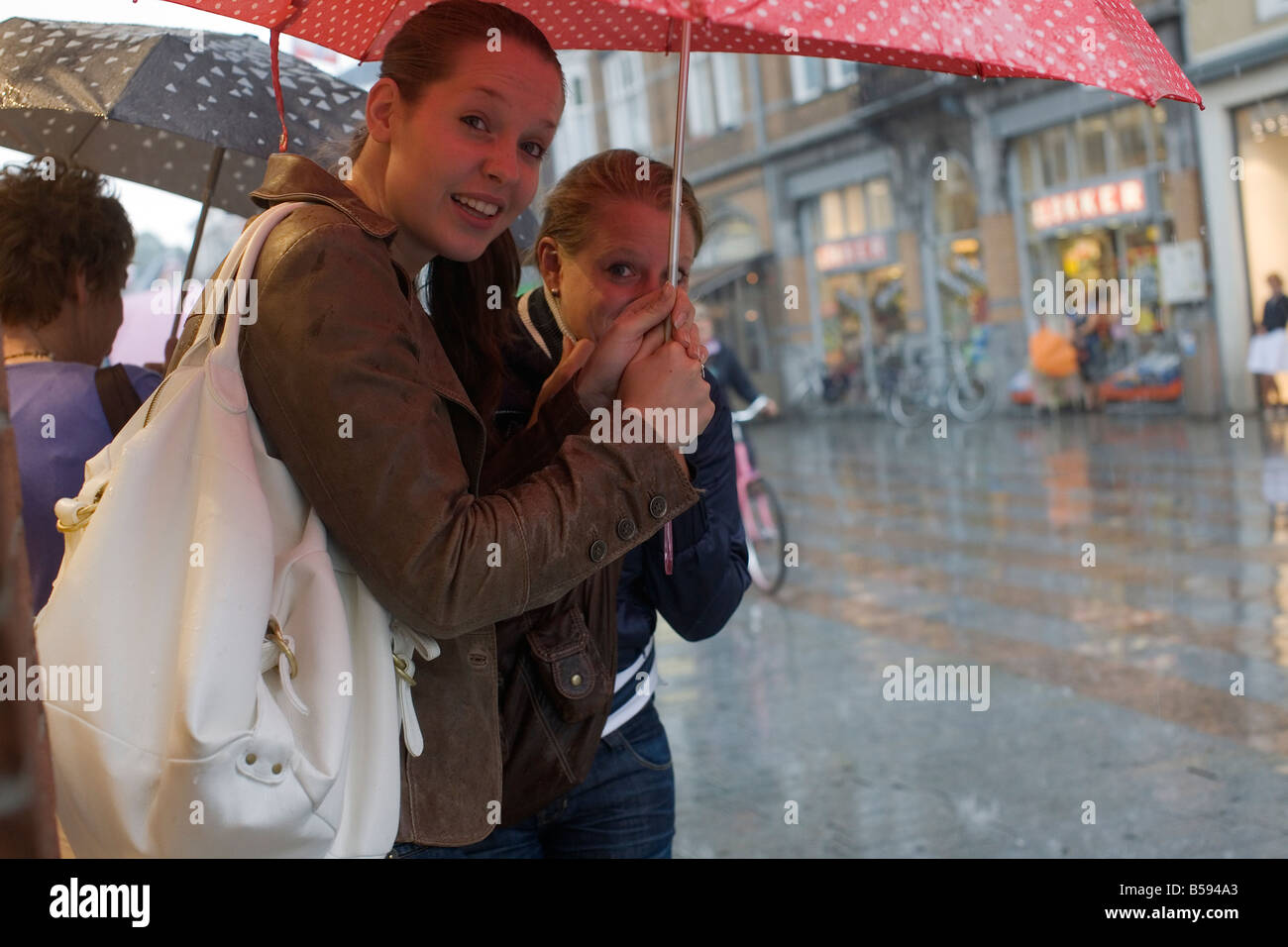 Two Girls sheltering under Umbrellas at a Rainshower. Stock Photo