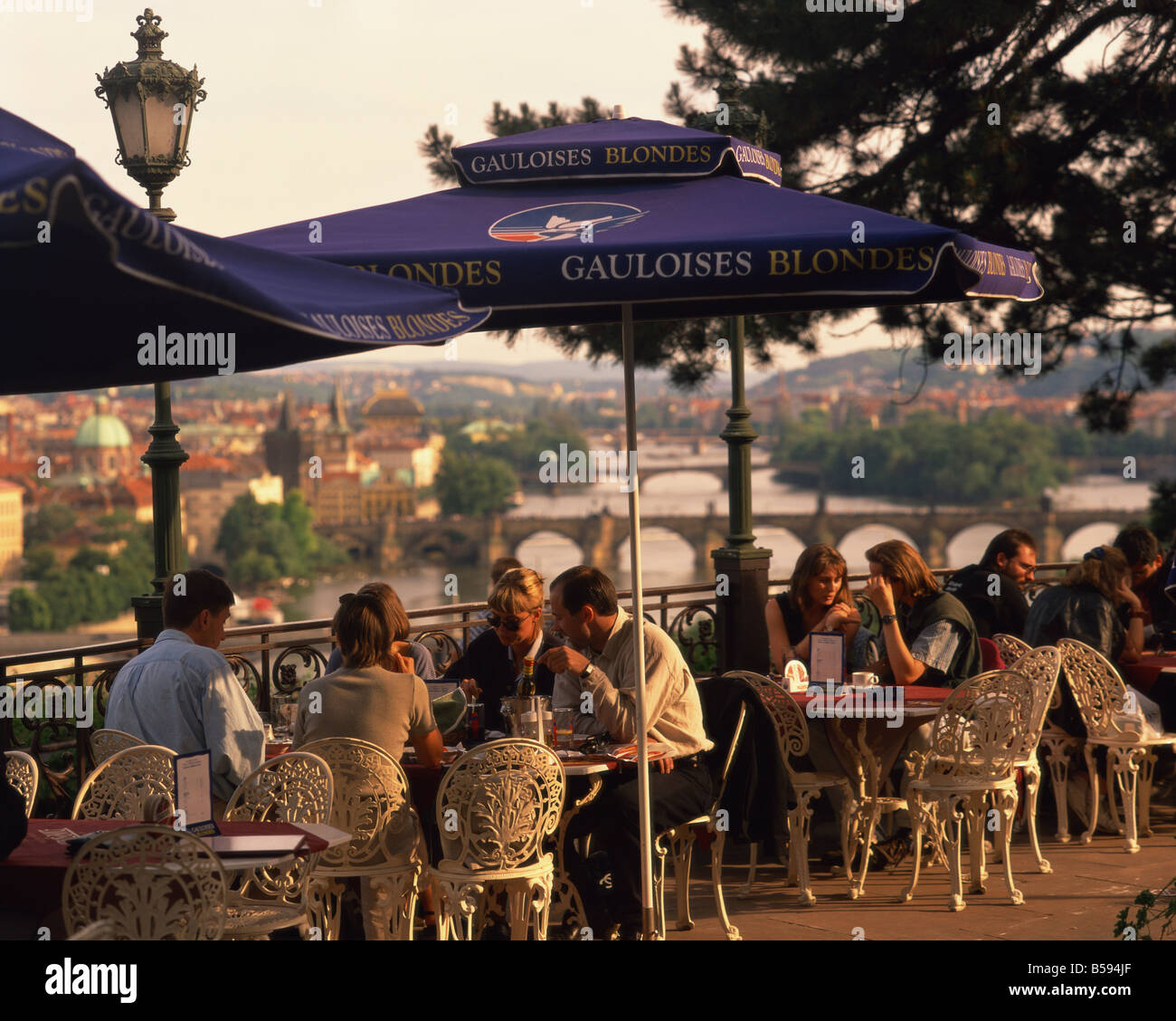 People at cafe tables in open air at the Hanavsky Pavilion, with the river and the city of Prague behind, in The Czech Republic Stock Photo