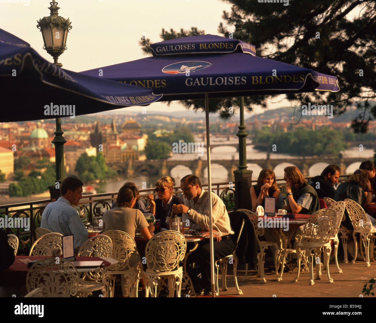 People at cafe tables in open air at the Hanavsky Pavilion, with the river and the city of Prague behind, in The Czech Republic Stock Photo