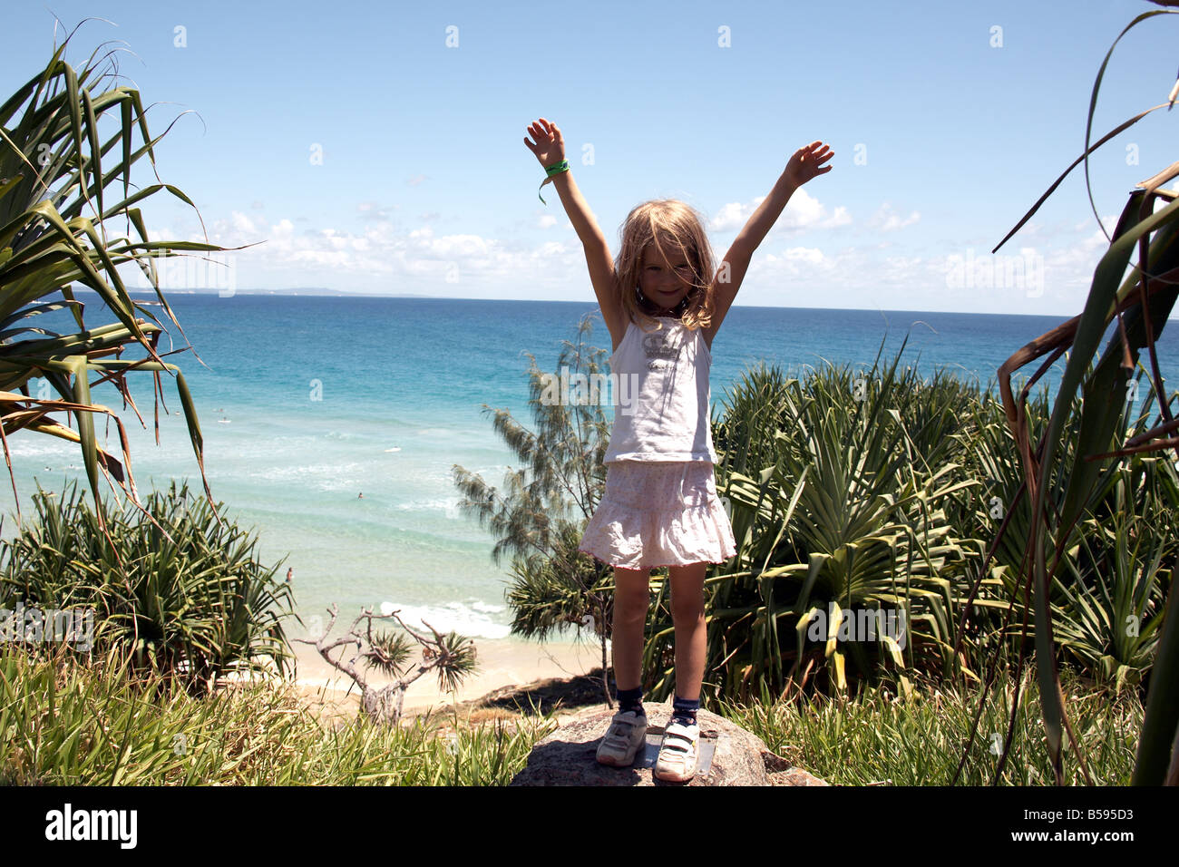 Young girl child happy celebration arms raised looking at sea at Cylinder Headland on North Stradbroke Island Queensland QLD Aus Stock Photo