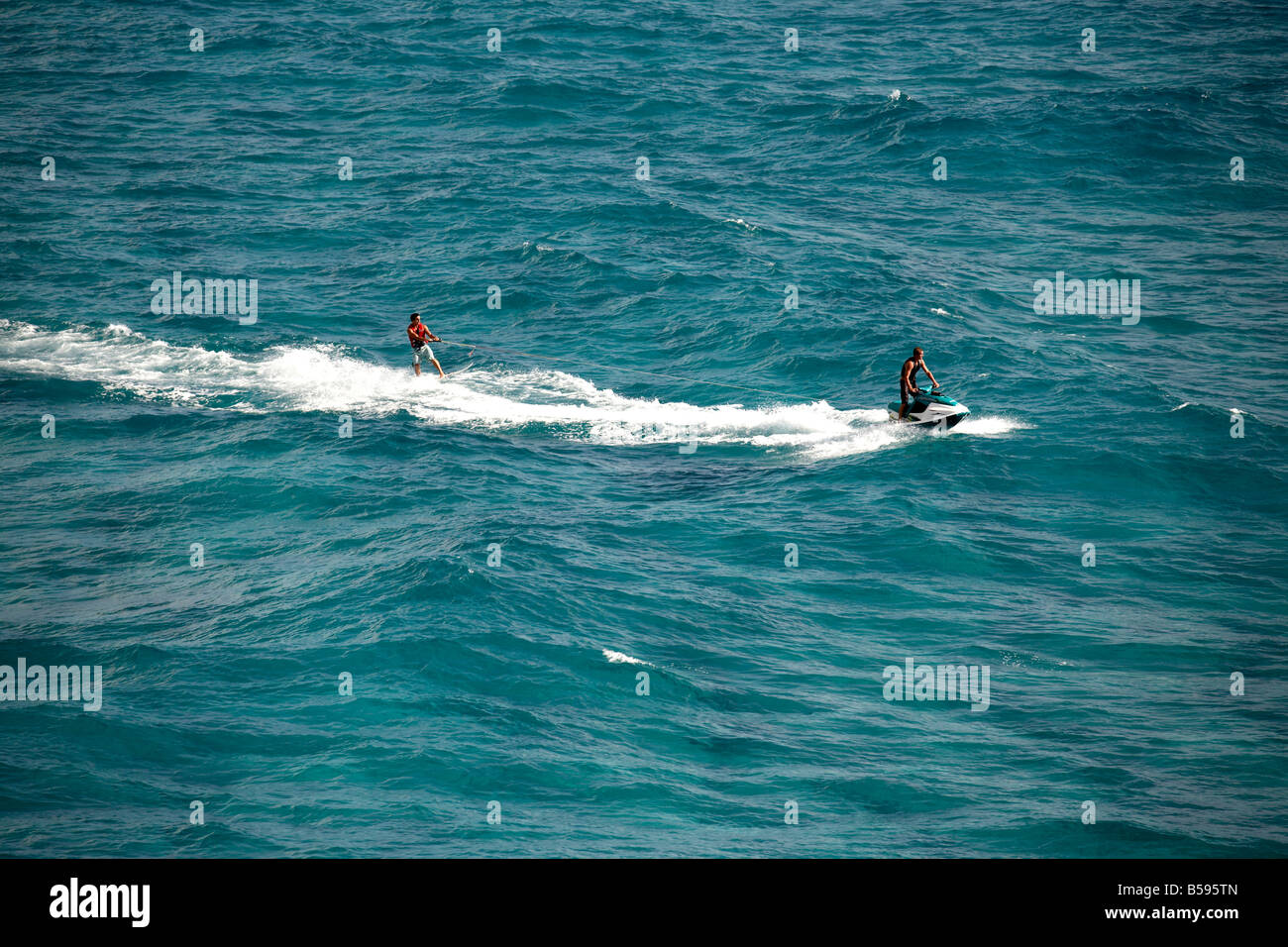 Waterskier on surf board water skiing being towed by man on jet ski in sea off North Stradbroke Island Queensland QLD Australia Stock Photo