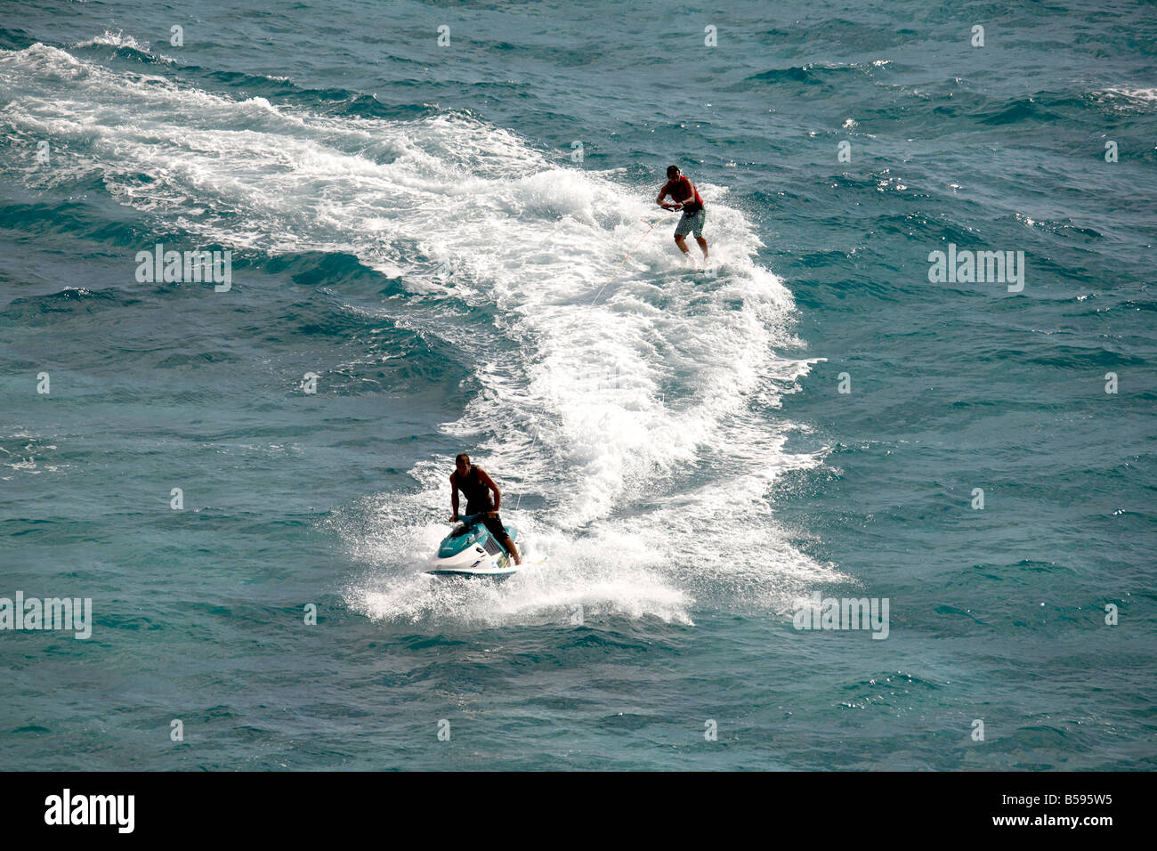 Waterskier on surf board water skiing being towed by man on jet ski in