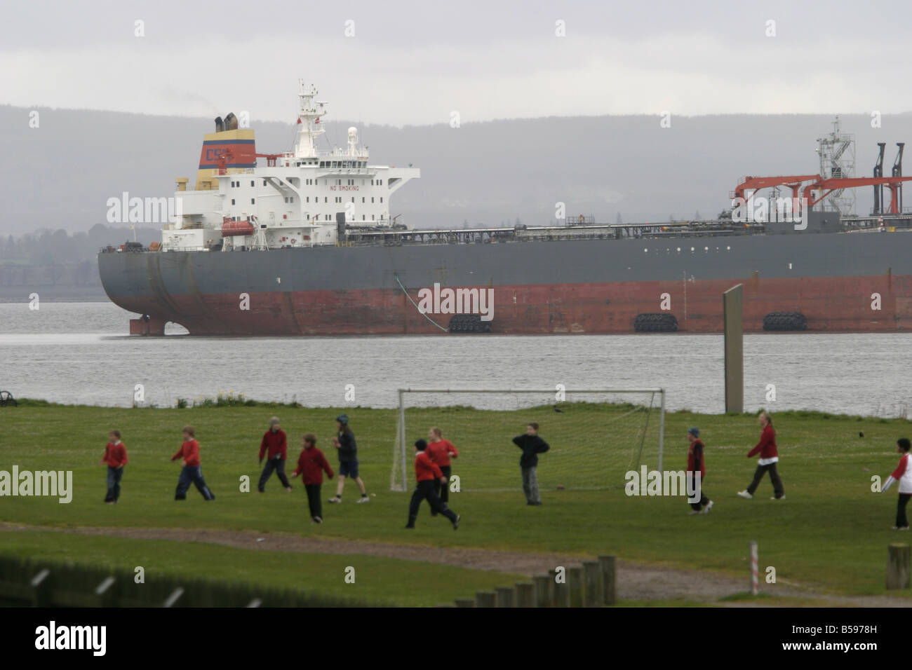 School children play football on the Links Cromarty while oil tanker loads up at Nigg oil terminal Stock Photo