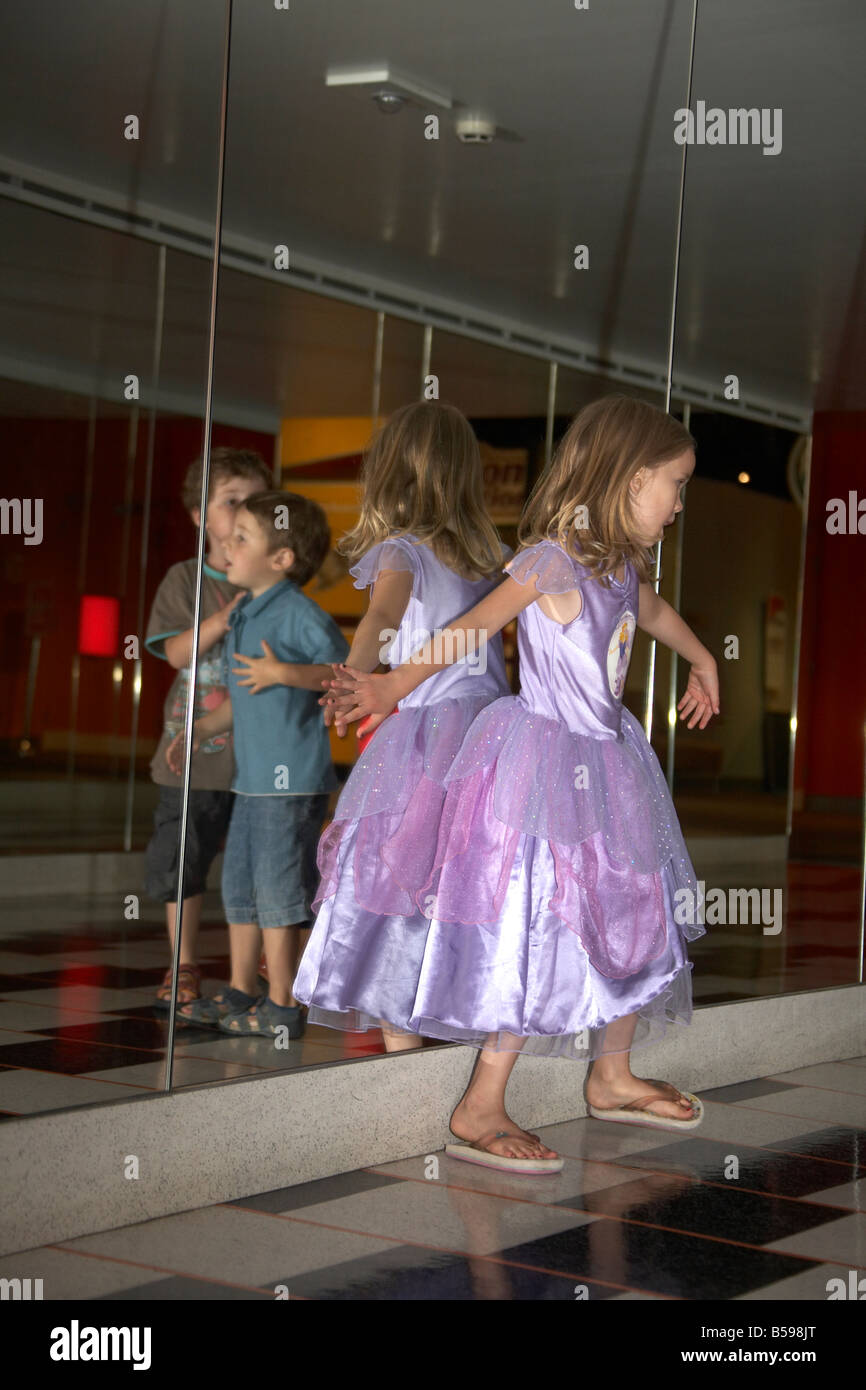 young girl in dress dancing in front of a mirror while young boy is