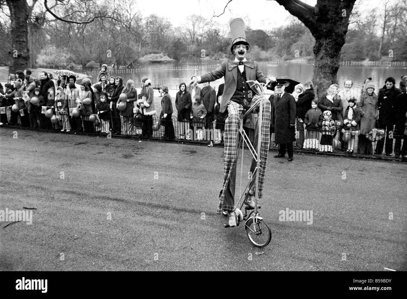 A clown stilt walker seen here riding a oversize bicycle in the  Easter parade, Battersea Park. March 1975 75-1706-001 Stock Photo