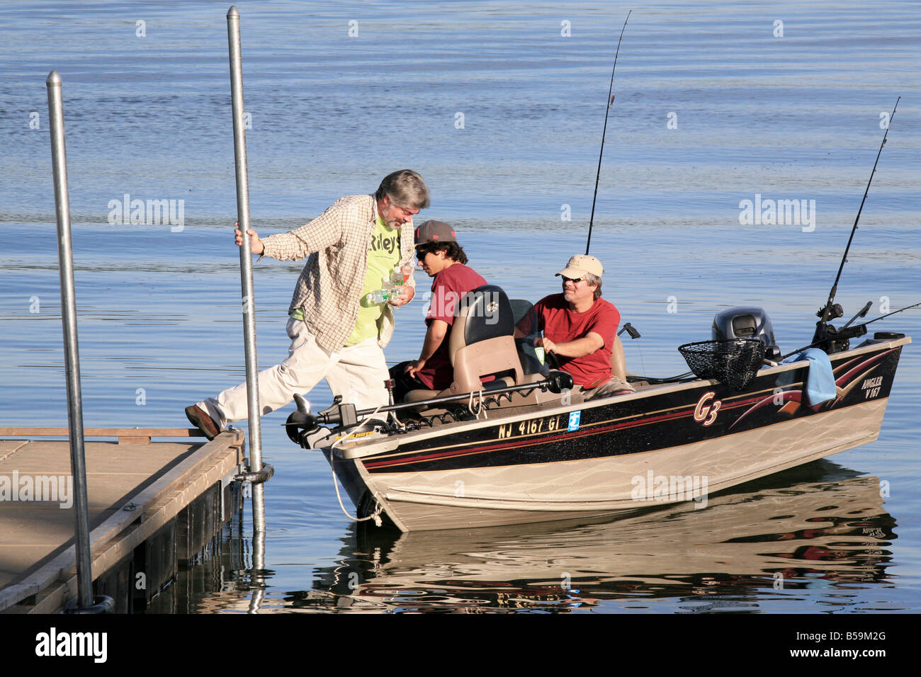 A fisherman stepping from the dock into a small fishing boat . Stock Photo