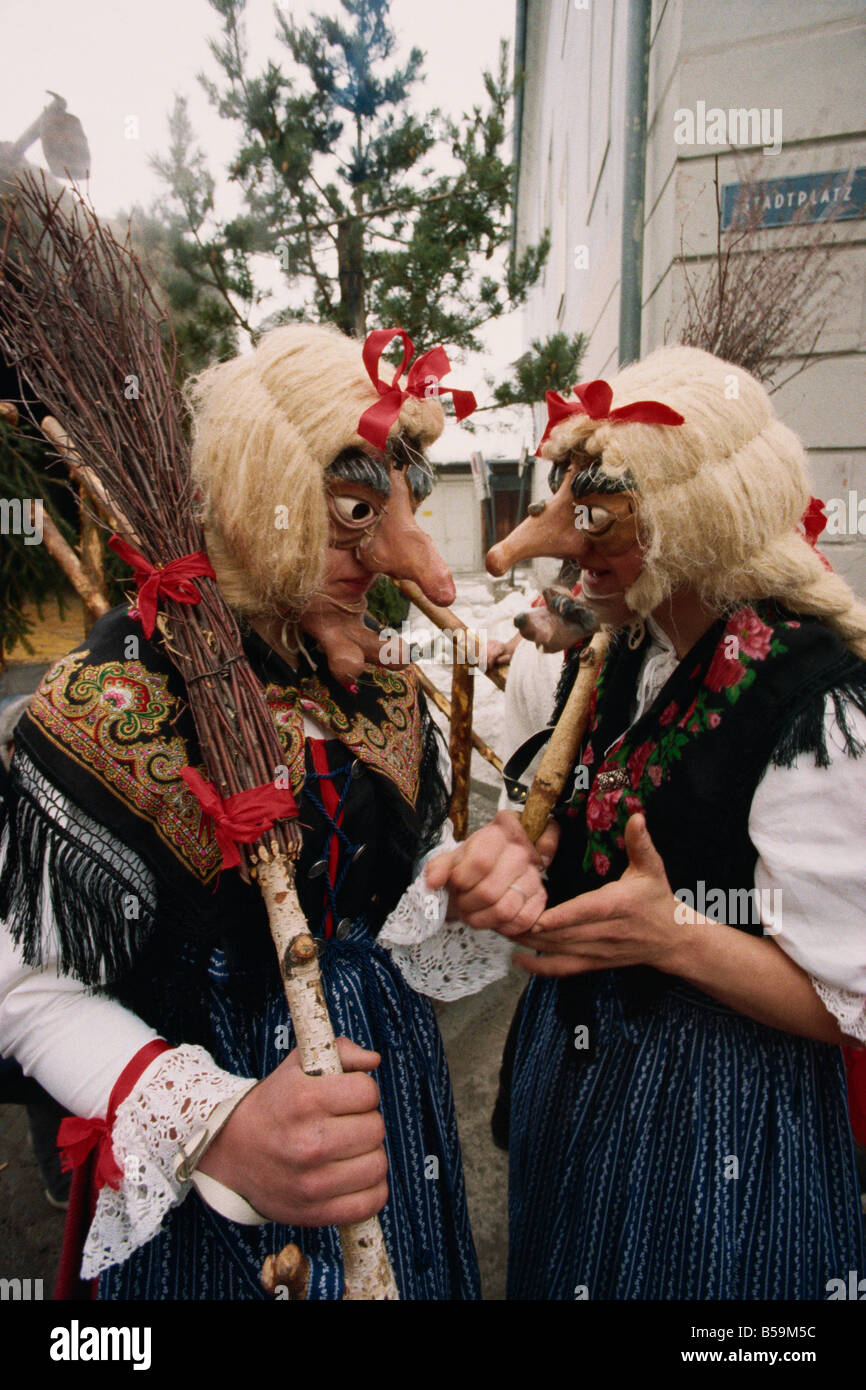 Two people wearing masks and traditional dress, one carrying a broomstick, in the Fasnacht carnival in Imst, Austria, Europe Stock Photo