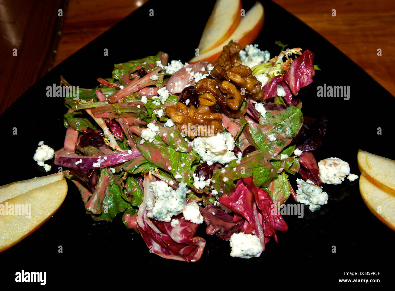 Green salad with arugula radicchio red onion endive topped with candied walnuts and blue cheese on a black plate Stock Photo