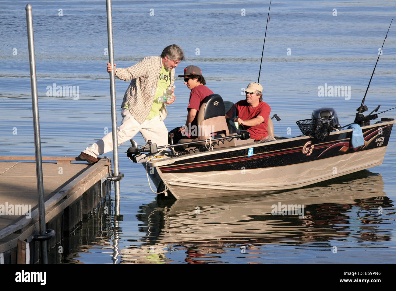 A fisherman stepping from the dock into a small fishing boat . Stock Photo