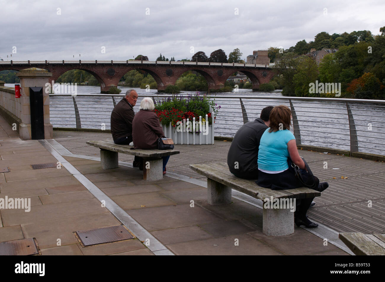 Young and elderly  couple sitting on bench by River Tay Perth Scotland UK Stock Photo