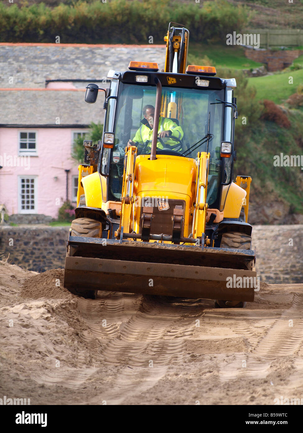 JCB digger moving sand back on to the beach from the path to the carpark. Summerleaze beach. Bude. Cornwall. Stock Photo