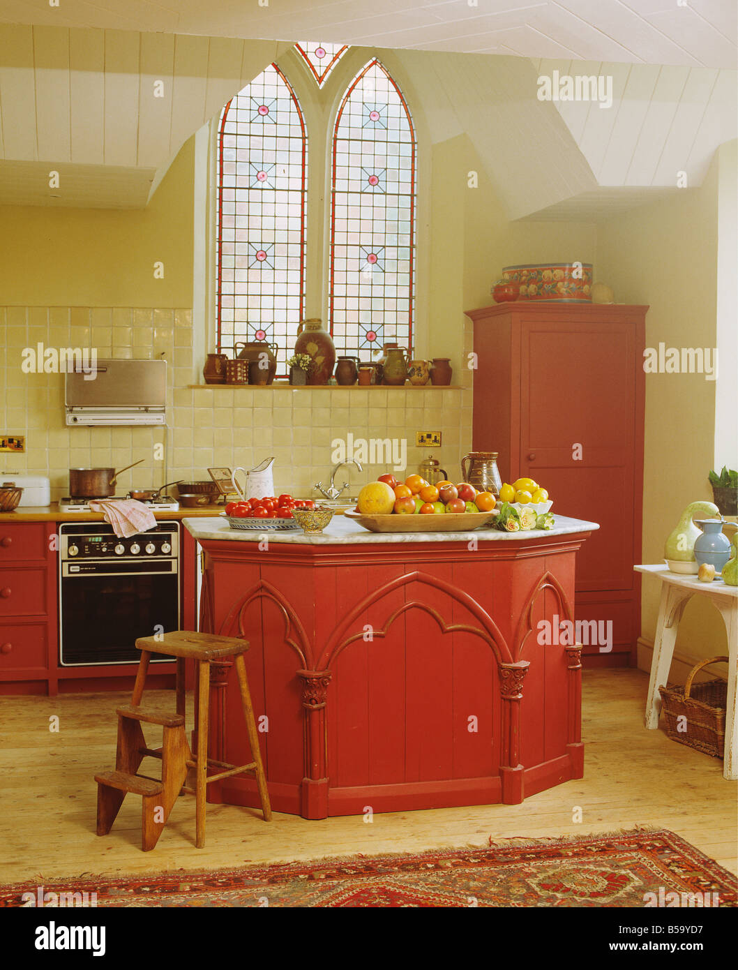Wooden steps beside red island unit in kitchen in converted church with ...