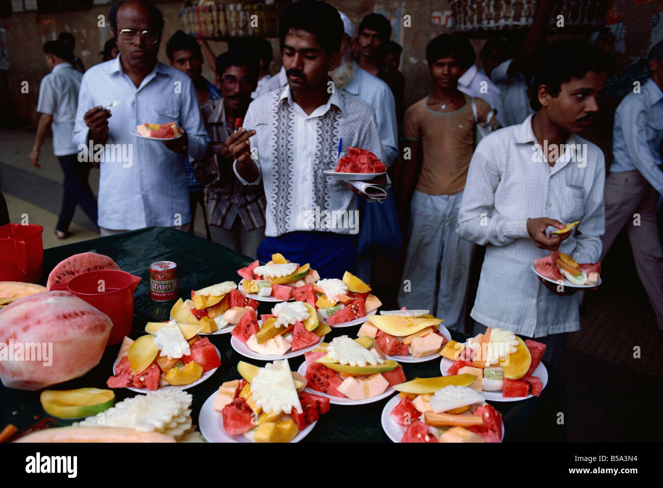 Three men enjoying a quick fruit salad on busy street Mumbai India Asia Stock Photo