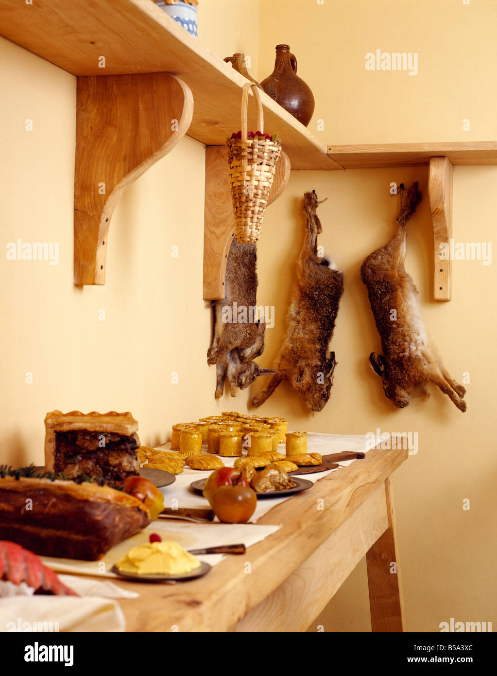 Wooden shelf with game rabbits above raised pies on wooden table in larder Stock Photo