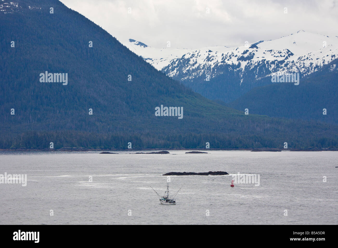 Commercial fishing boat trawling the waters of Inside Passage between Seattle and Alaska in front of snow capped mountains Stock Photo