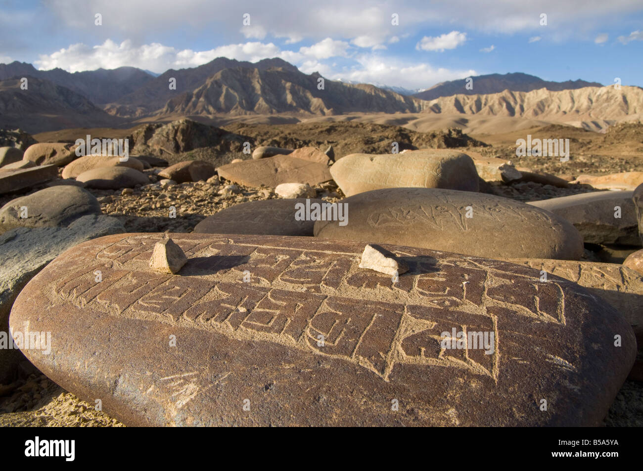 Close up of traditional carved prayer stones on a prayer wall with desert landscape and mountains beyond, Alchi, Ladakh, India Stock Photo