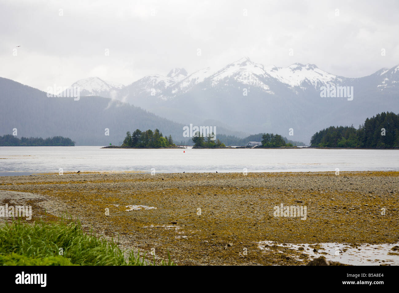 Private island home between snow capped mountains and the Eastern Channel shoreline in Sitka, Alaska Stock Photo