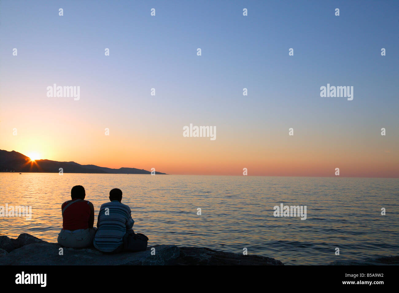 Couple sitting on sea wall watching sunset Stock Photo - Alamy