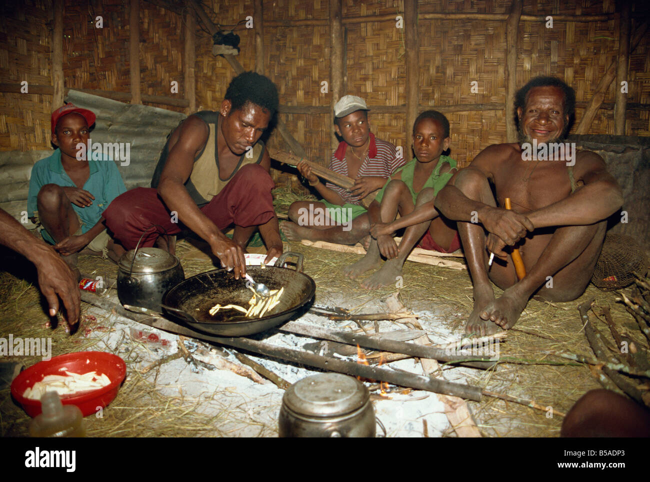 Dani men inside house, preparing dinner and playing wooden guitar, South Beliam Valley, Irian Jaya, Indonesia, Asia Stock Photo