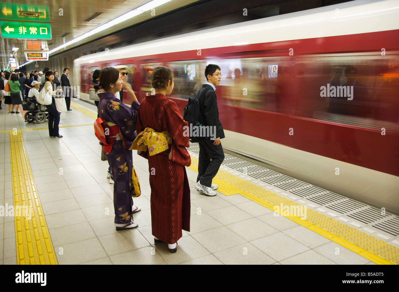 Young women in traditional kimono waiting gracefully for train at Kyoto station, demonstrating proper kimono etiquette for public transportation