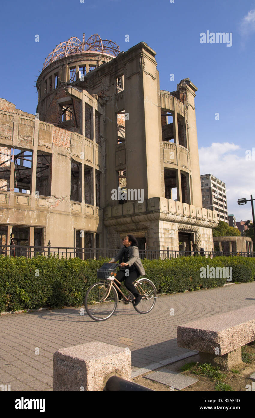 Woman riding bicycle past A Bomb Dome, the ruins of the Industrial Promotion Hall, Hiroshima, Honshu, Japan Stock Photo