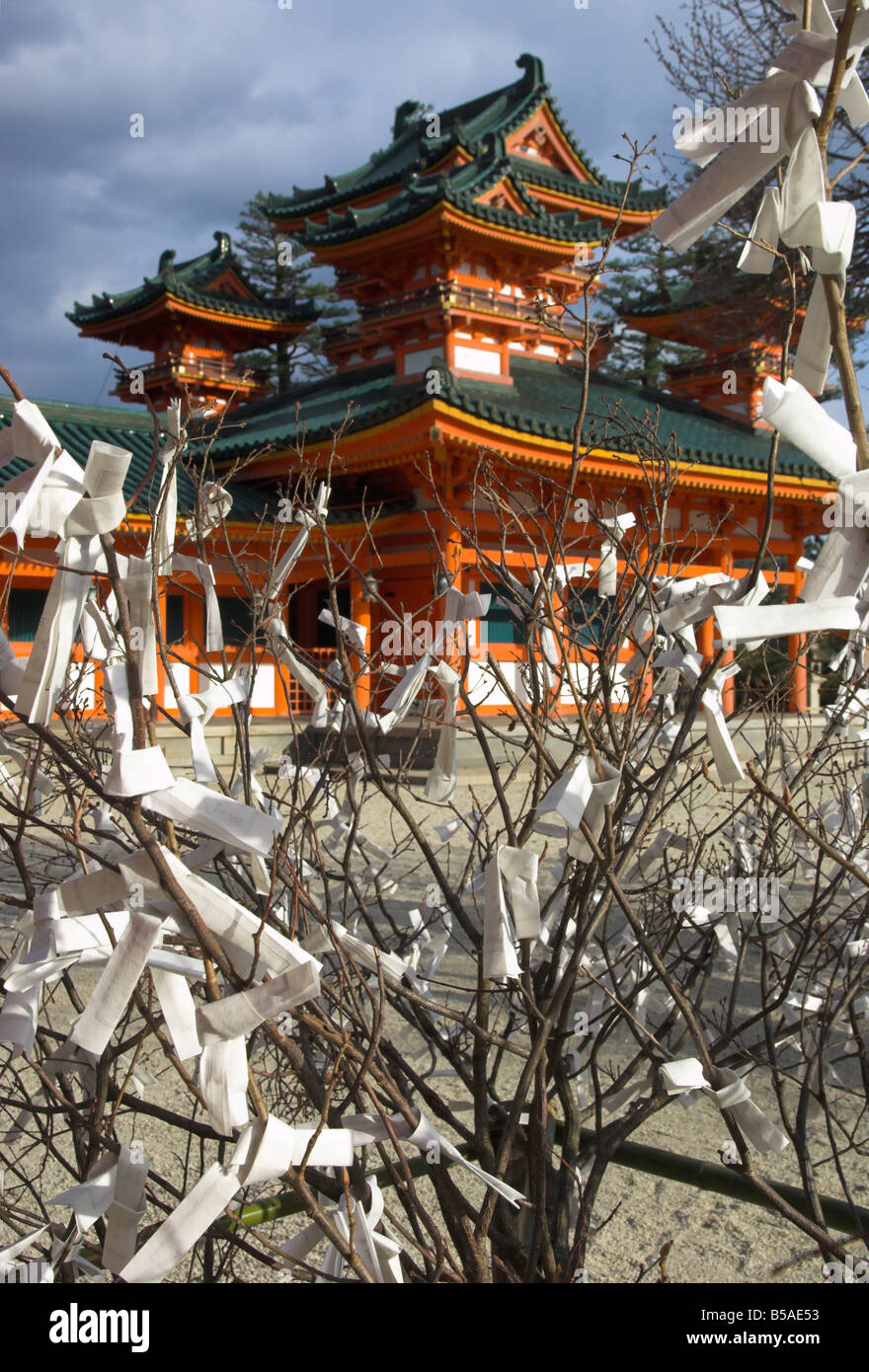 Fate and wish papers tied on a bush branches in foreground and temple beyond, Heian Jingu shrine, Kyoto, Kansai, Honshu, Japan Stock Photo