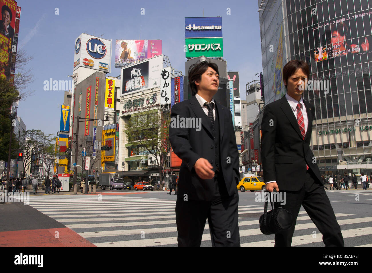Well dressed young men walking on zebra crossing with advertising posters and huge, Shibuya, Tokyo, Japan Stock Photo