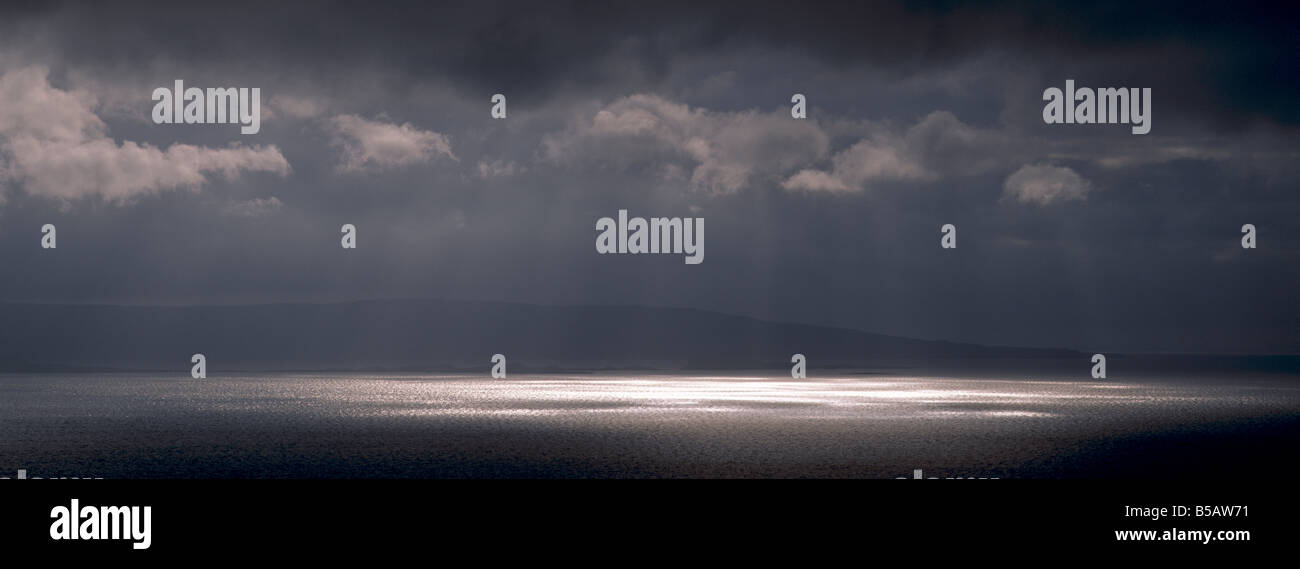 Sun breaking through stormy overcast sky over calm water Stock Photo