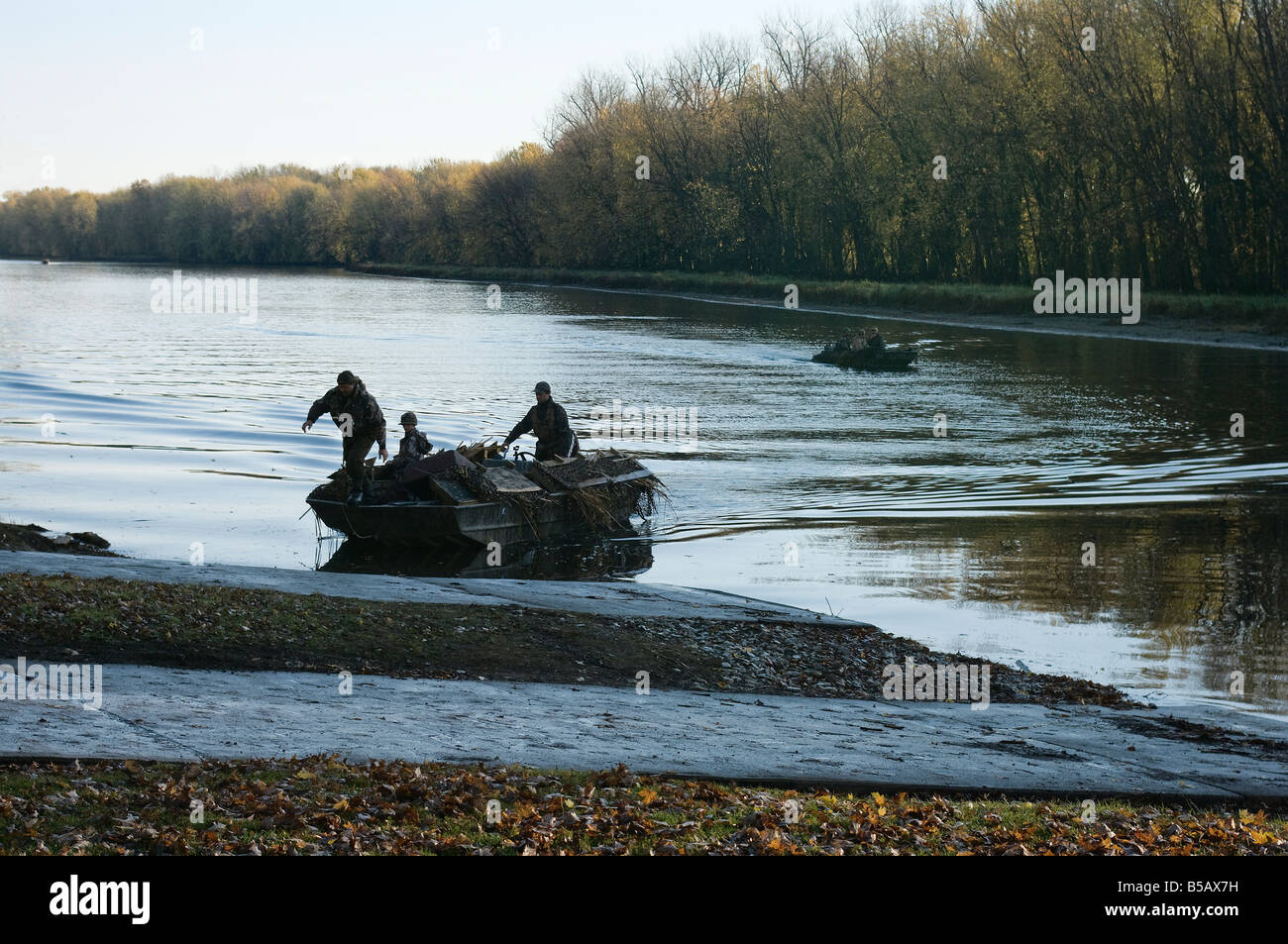 Duck hunters in camouflage landing in a camouflaged boat during bird hunting season Stock Photo