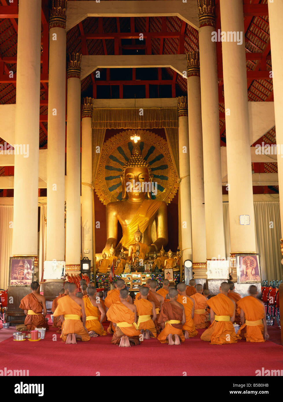Monks in saffron robes kneel before a statue of the Buddha in Wat Praising in Chiang Mai Thailand Asia C Boonsom Stock Photo