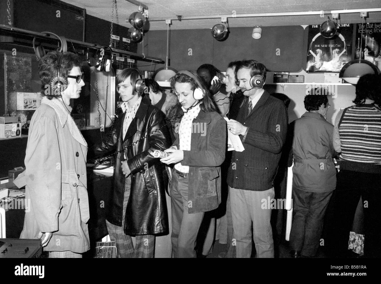 Beat the Budget shopping spree in Tottenham Court Road, London, street of radio and Hi-fi. ;Customers trying on headphones in an electrical store;April 1975 ; Stock Photo