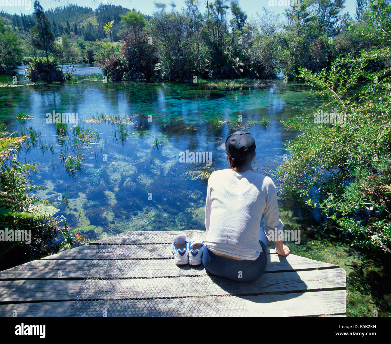 A tourist sitting on the edge of Pupu springs largest freshwater spring in New Zealand at Golden Bay South Island New Zealand Stock Photo