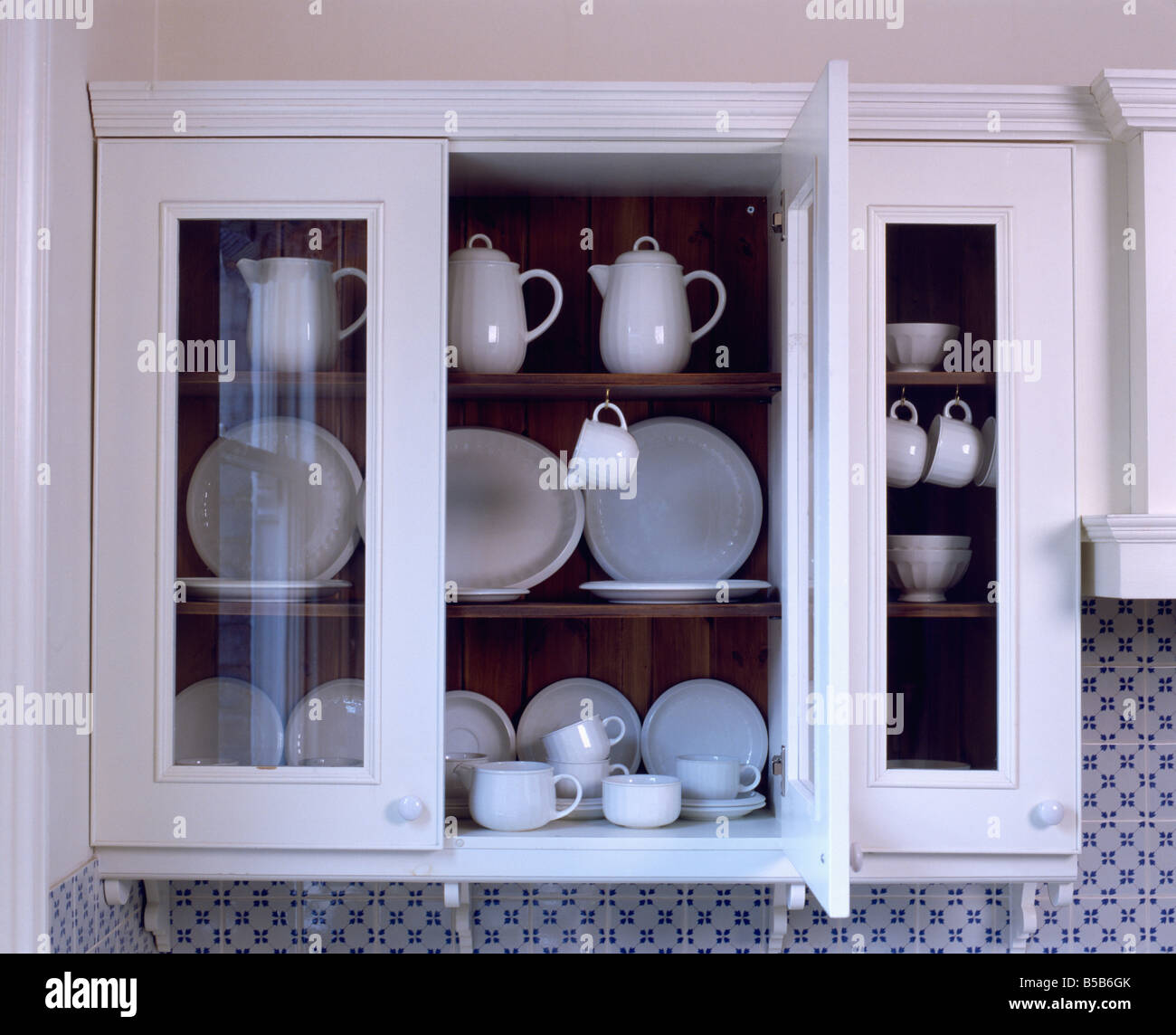 White wall cupboard with glass doors open to reveal white crockery on  shelves Stock Photo - Alamy
