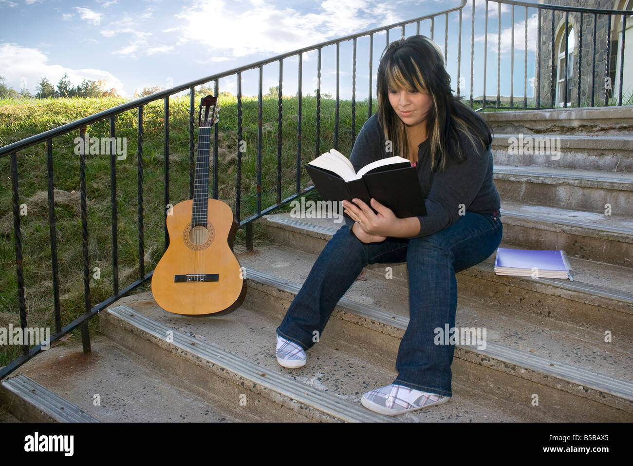 A young woman with highlighted hair reading a book or doing homework on campus Stock Photo