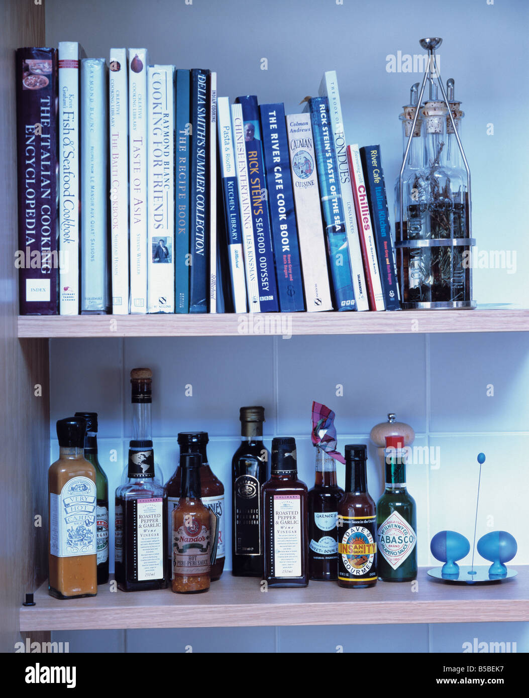Close-up of cookery books and bottles of relishes and sauces on white shelves Stock Photo