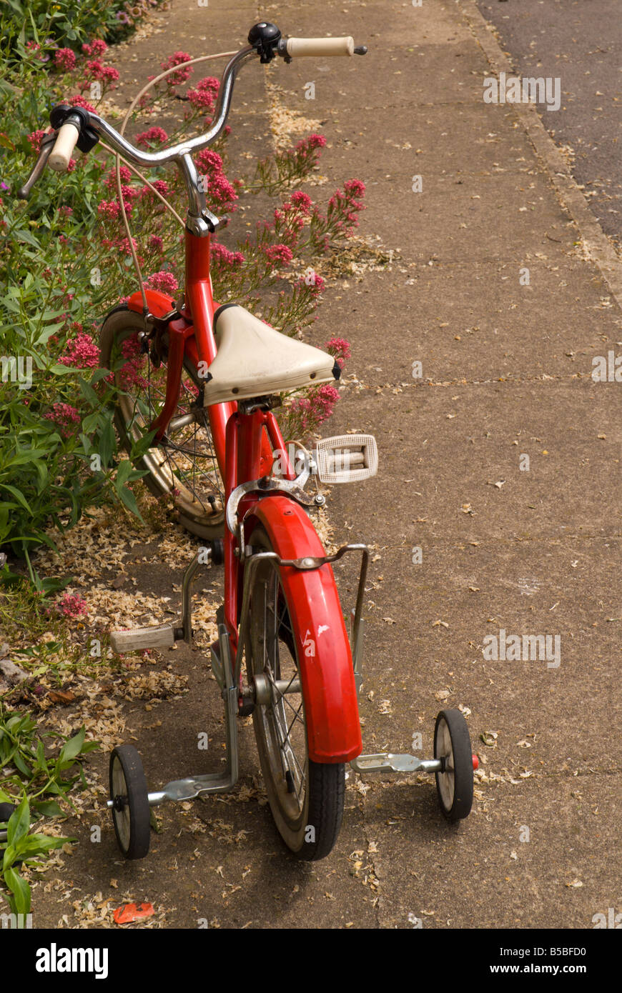 An old fashioned red child's bicycle with training wheels on the