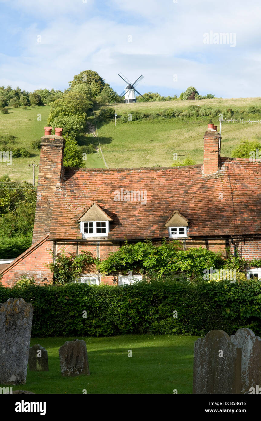 Country cottage in a village with a windmill on the hill in the background on a sunny day close up Stock Photo