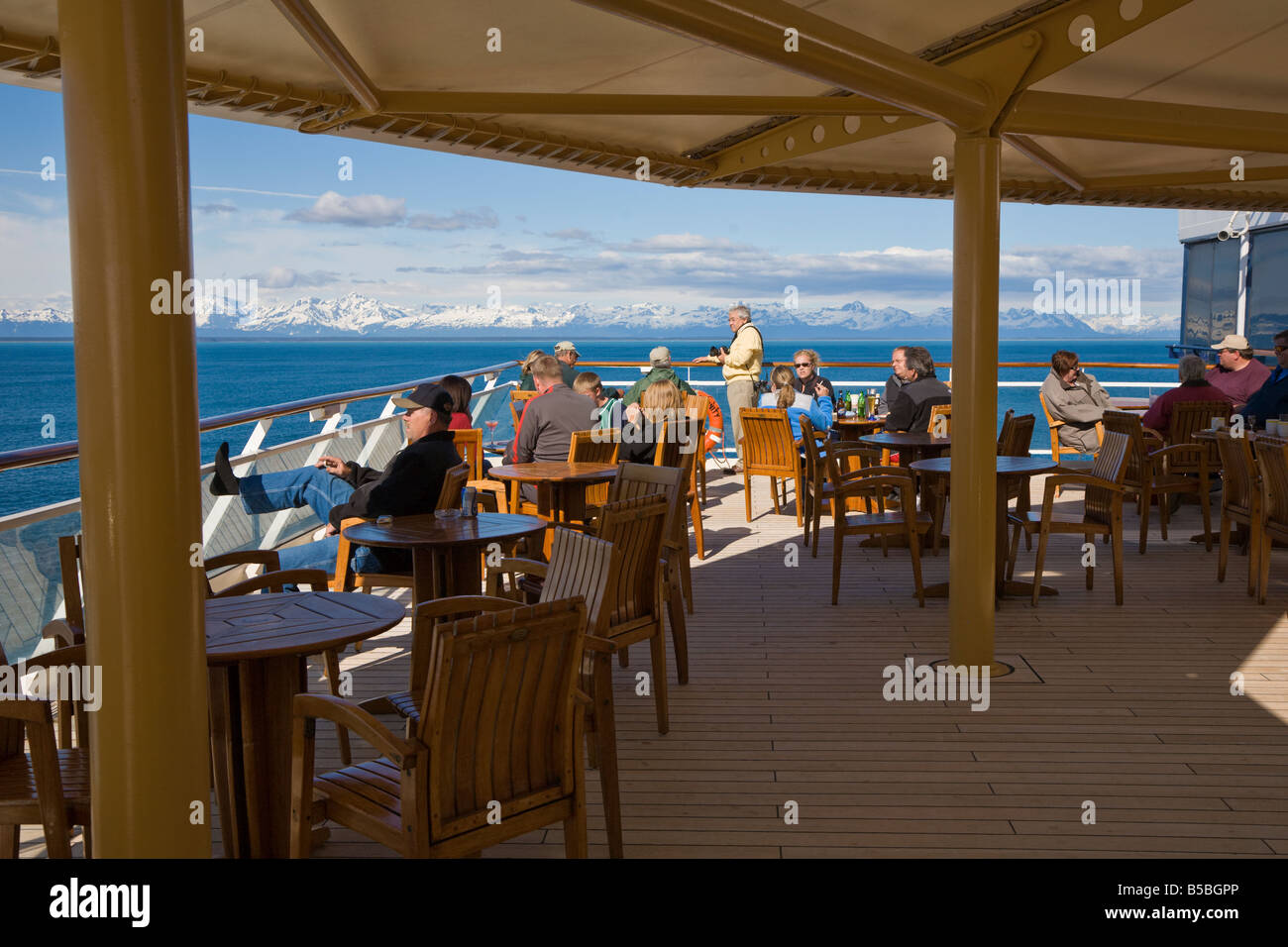 Cruise passengers visiting on outdoor dining deck watching snow capped mountains on Inside Passage cruise in Alaska Stock Photo