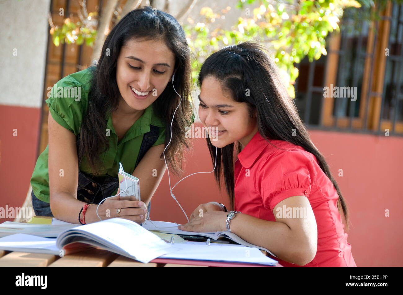 School teenage girl asian students 15-17 years sharing earphones with their Mp4 iPod player outside in sunny school playground campus Stock Photo