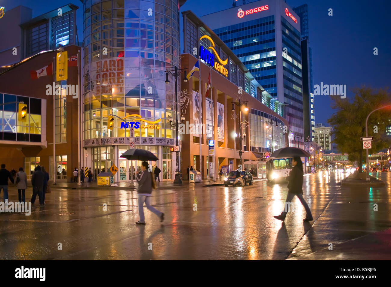 Pedestrians crossing a city street on a rainy night, carrying umbrellas, Portage Avenue, Winnipeg, Manitoba, Canada. Stock Photo