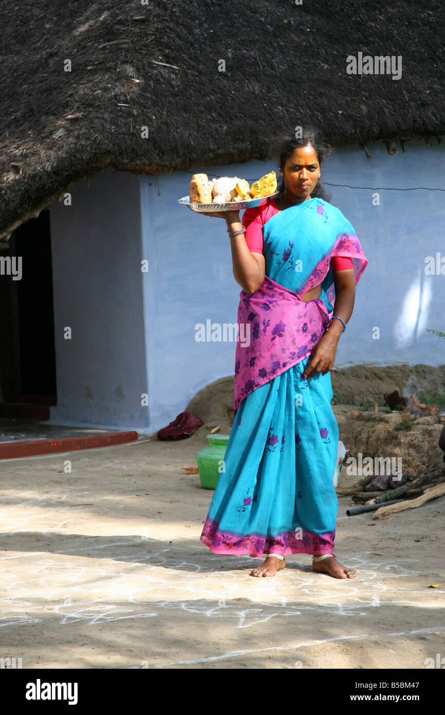 a-woman-stands-outside-of-her-thatched-h