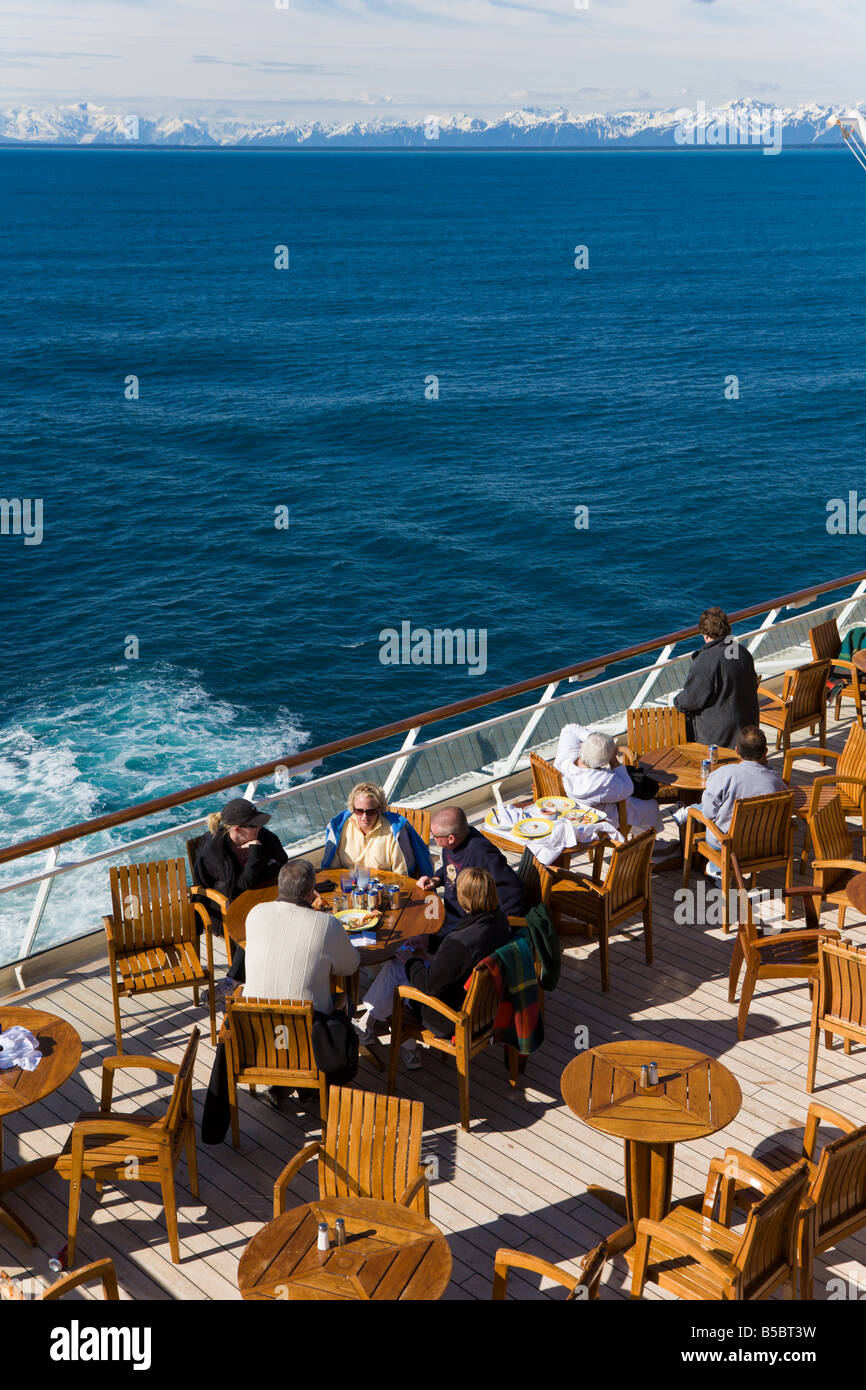 Cruise passengers visiting on outdoor dining deck watching snow capped mountains on Inside Passage cruise in Alaska Stock Photo