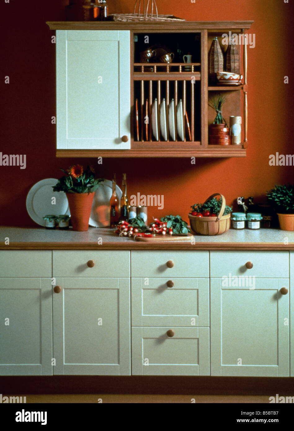 Plate rack and wooden shelves on wall unit in red kitchen with white fitted cupboards Stock Photo