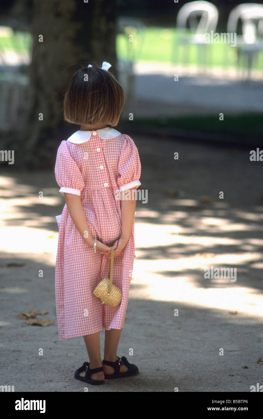 Little girl in a pretty red checked dress and bow in her hair in a park Stock Photo