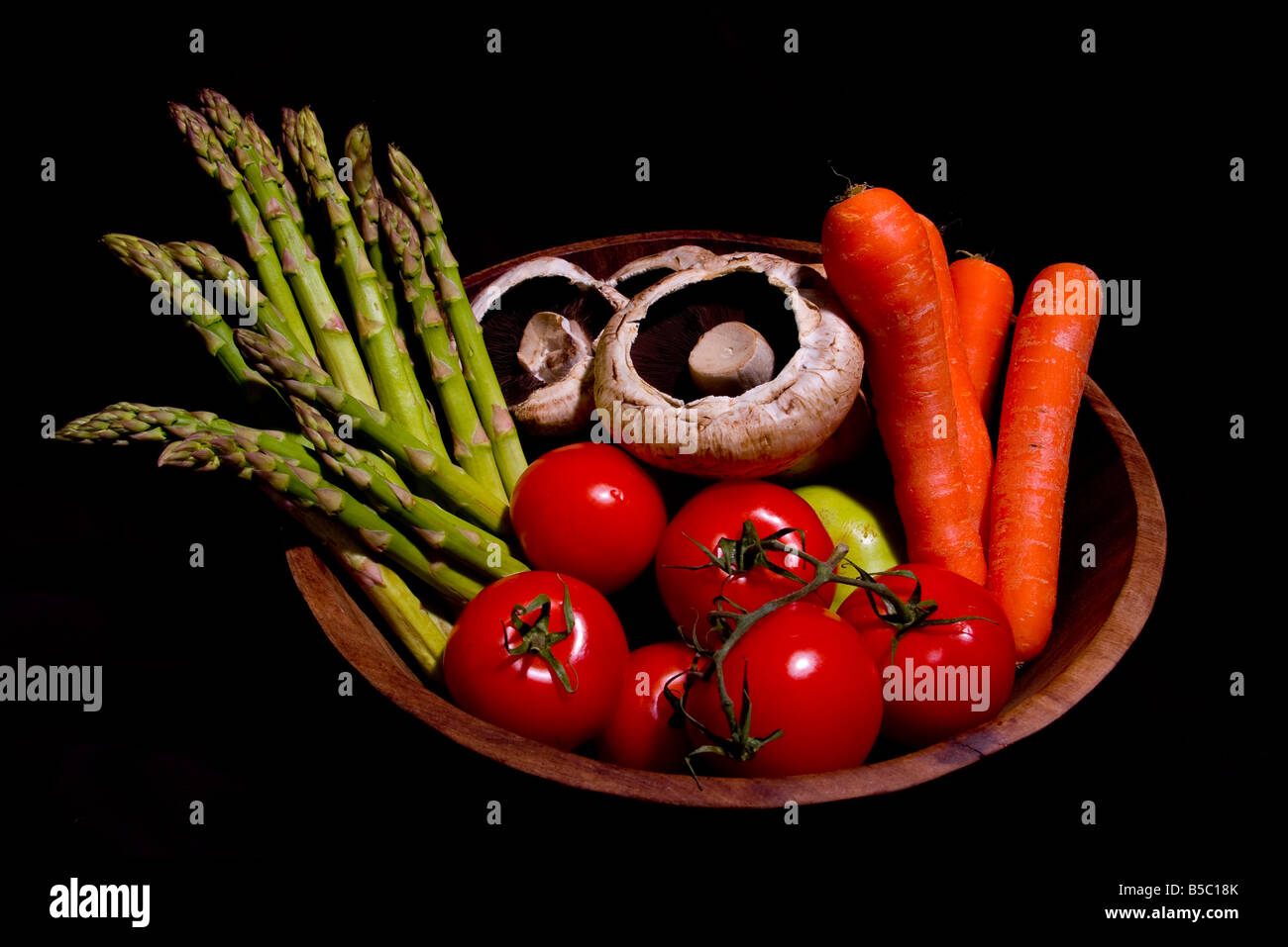 Healthy homegrown organic genuine color vegetables tomatoes mushrooms asparagus carrots in a wooden bowl with black background Stock Photo
