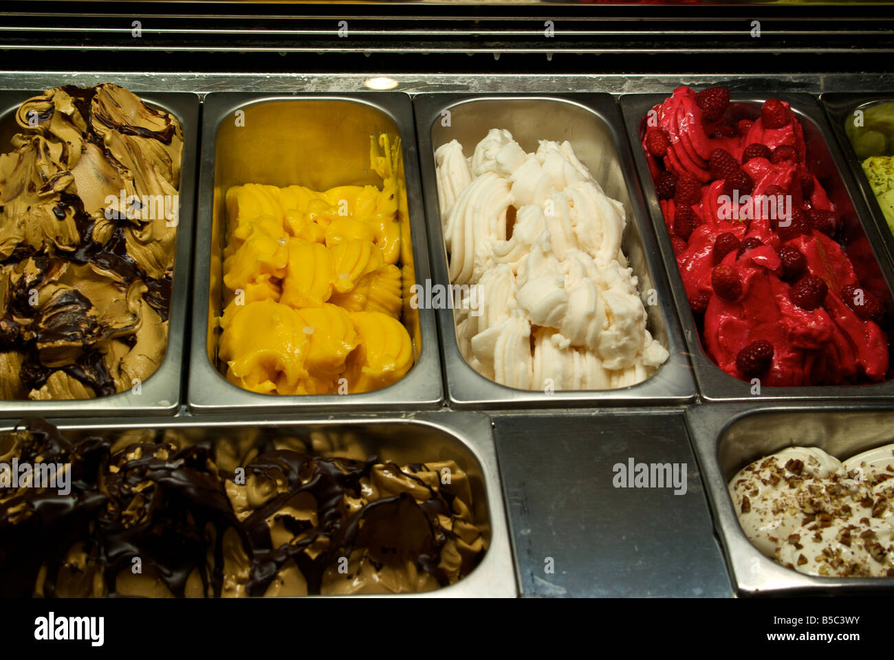 Stainless steel tubs of fancy gelatos in ice cream freezer display case Stock Photo