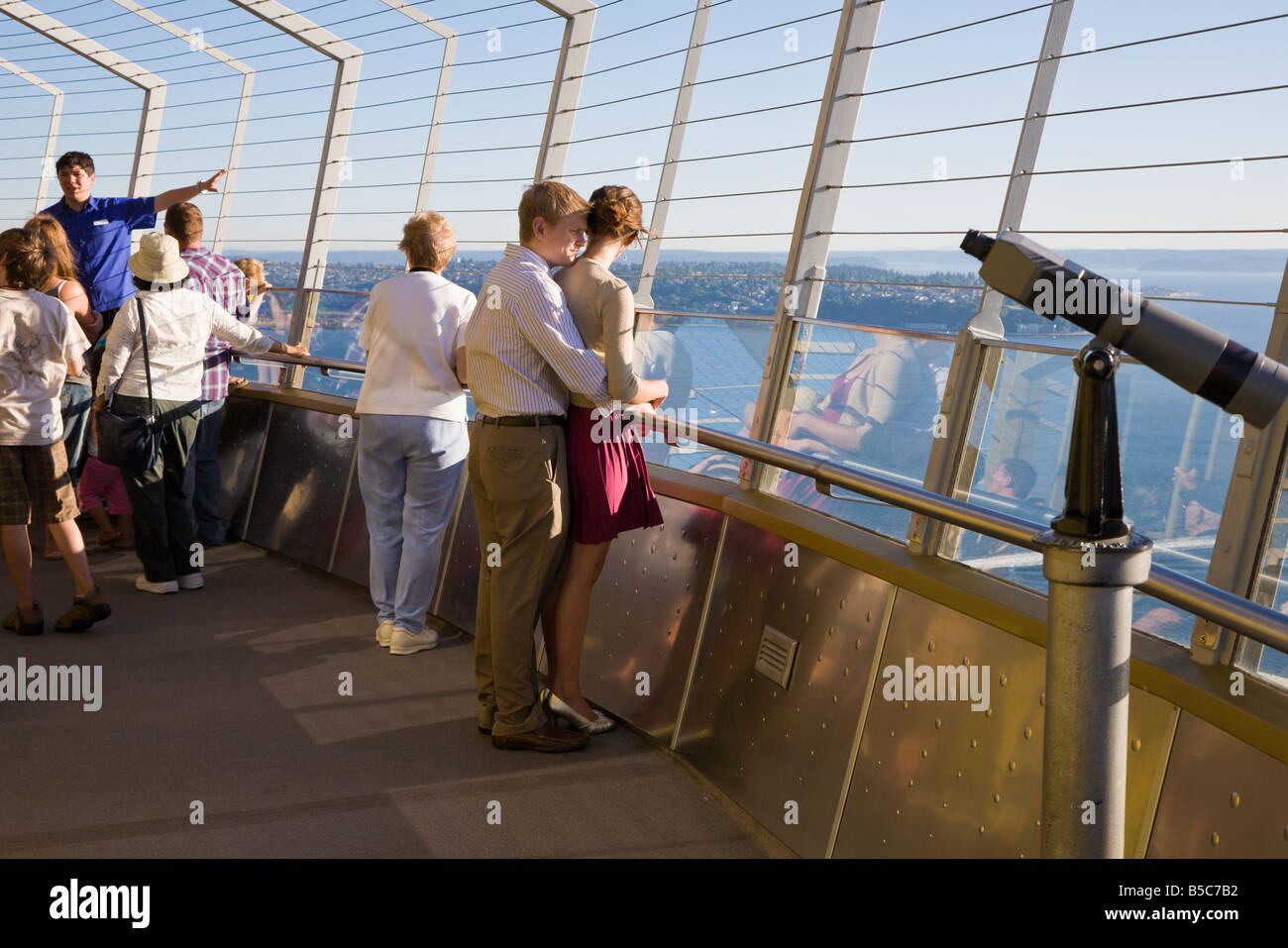 Romantic couple stand together while tour guide talks to visitors on the observation deck of the Space Needle in Seattle, WA Stock Photo