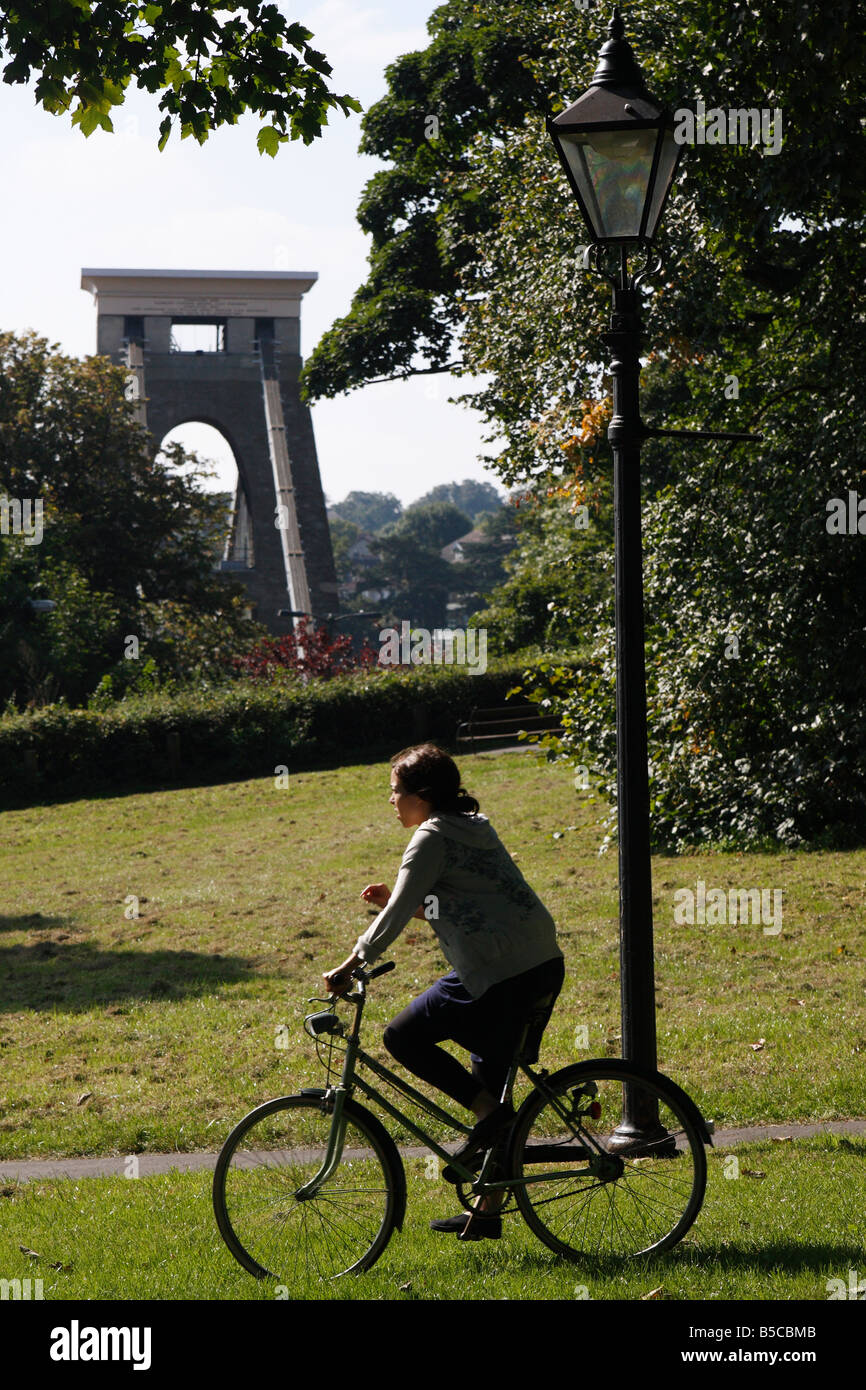 Woman cycling through public park with [Clifton Suspension Bridge] in background, 'Clifton Down', Bristol, England, UK Stock Photo