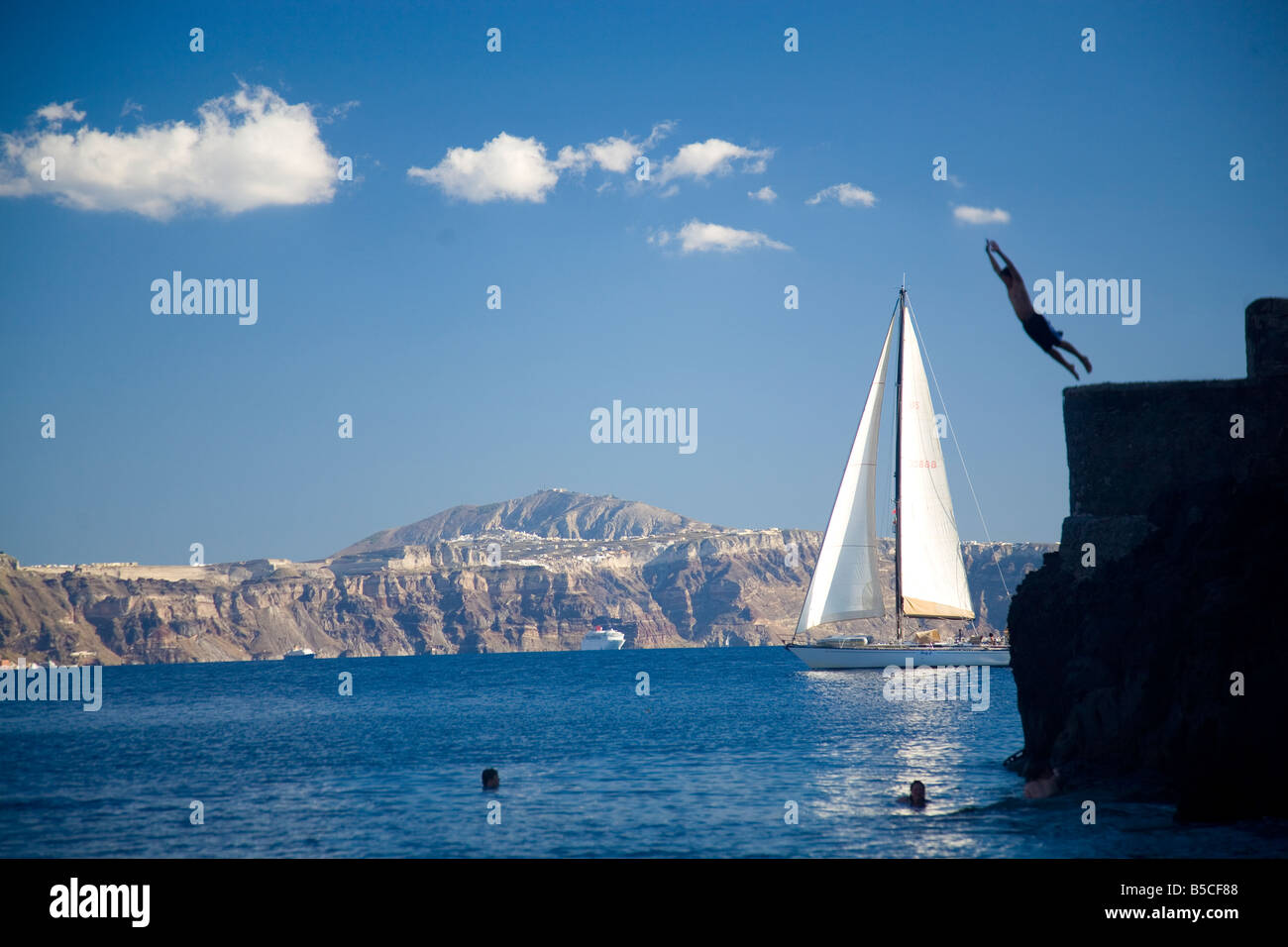 Amoudi Bay Santorini Greece man jumping off edge sail boat coming into