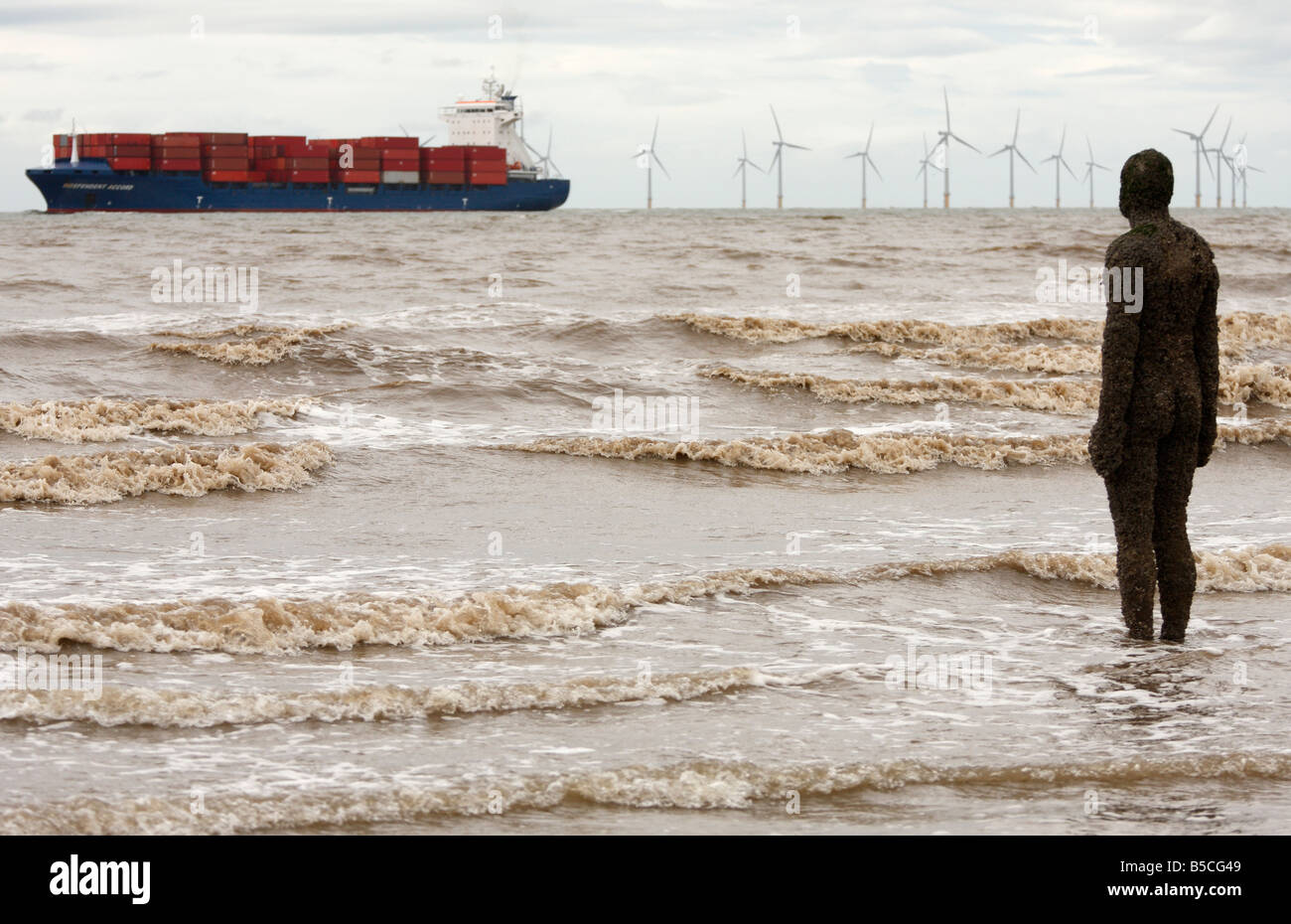 Antony Gormley sculpture of man in sea looking at passing ship and 'Burbo Bank' offshore  'wind farm', Crosby Beach, England, UK Stock Photo